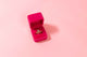 A bright pink velvet ring box is open with two gem encrusted rings stacked on top of each other, the top ring is teardrop shaped with an opal stone inlay and the bottom ring is shaped like the bottom half of a 5-point star