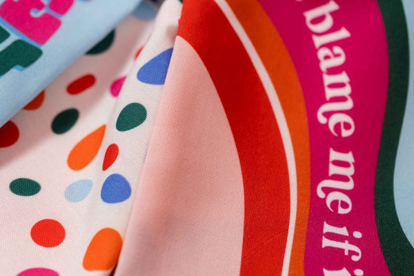 Set of three brightly colored tea towels with scalloped edges each with a different design, a light blue towel with a groovy font repeatedly reads house party, a white towel with multi-colored abstract dots, and a blush pink towel with a multi-colored wave design