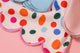Macro view of white tea towel with multi-colored abstract dots and pink scalloped edge detailing