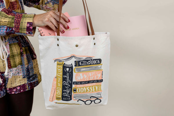 Cream colored tote bag with leather handles featuring illustration of classic books. Perfect gift for a reader.
