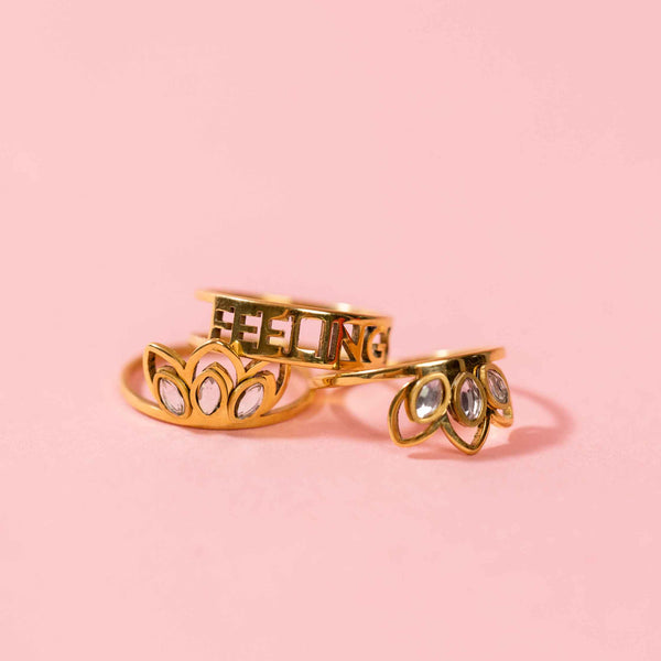 Closeup view of set of three gold rings, two rings feature three pointed detailing with marquis-shaped stones and one reads Feelings