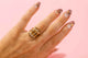 Closeup view of a hand wearing a set of three gold rings stacked on top of each other, the center ring reads Feelings and the rings on top and bottom feature pointed detailing with three marquis-shaped stones