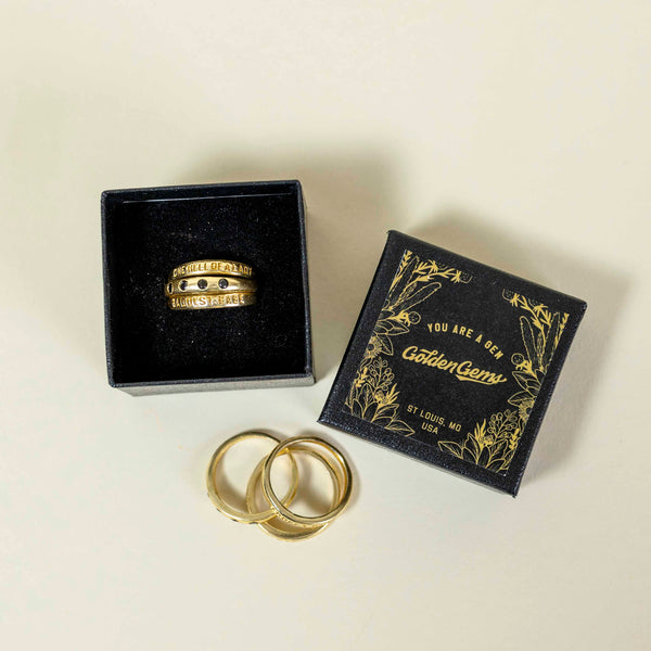 Set of three gold plated band rings, one with phrase Baddest Babe, one with phrase One Hell Of A Lady, one with four black gemstones around the band, made by Golden Gems 