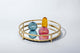 Gold circular bamboo tabletop tray with mirror bottom, featuring a yellow bud vase, pink bud vase, and blue bud vase